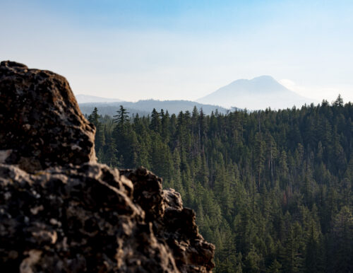 Rocky ridge overlooking dense forest and distant Three Sisters volcano in Oregon